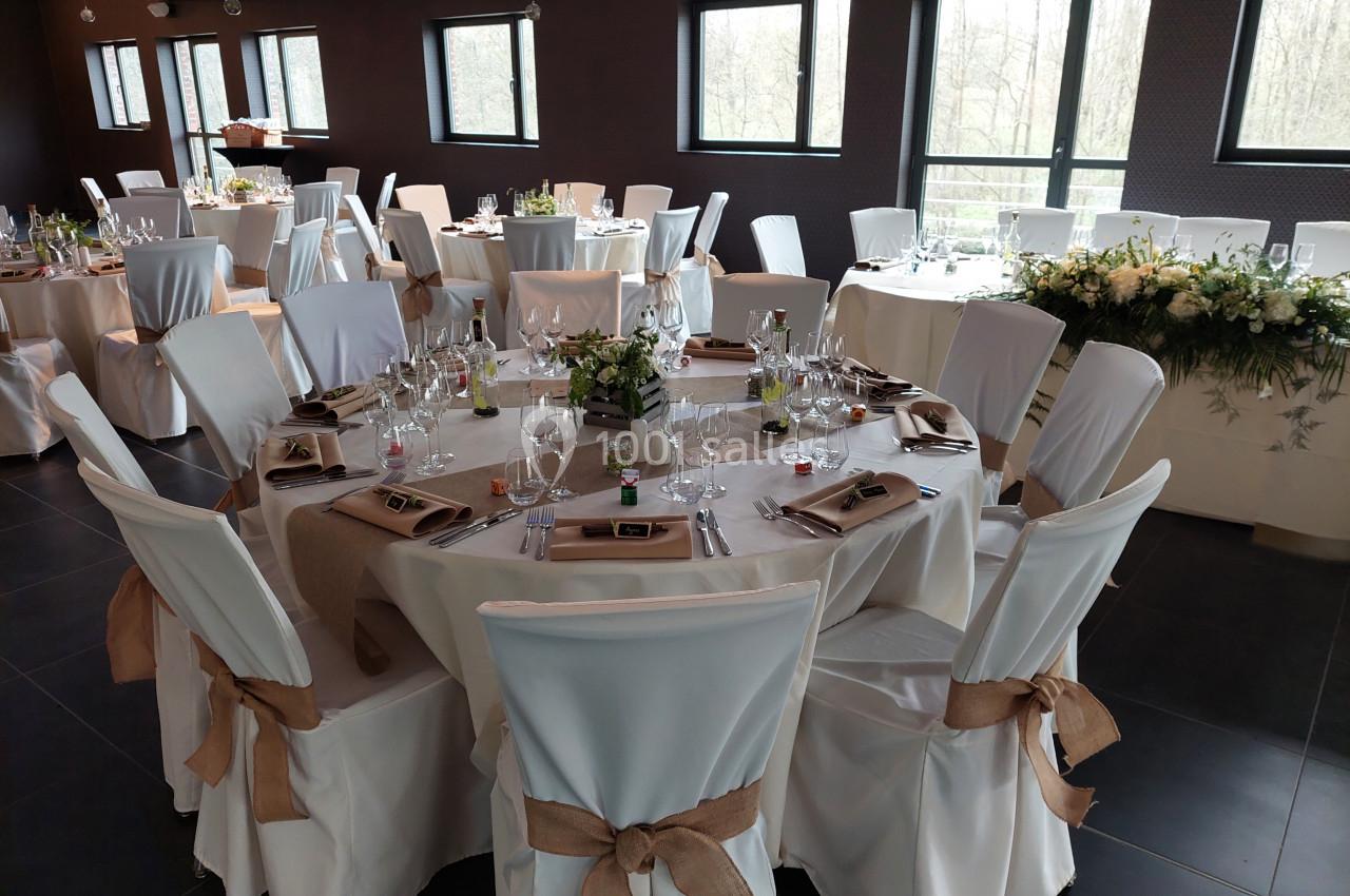 Salle de réception décorée avec des tables rondes élégamment dressées, nappes blanches et chaises ornées de rubans.