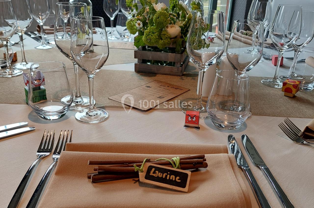 Table élégamment dressée avec serviette beige, couverts, verres et décoration florale au centre.