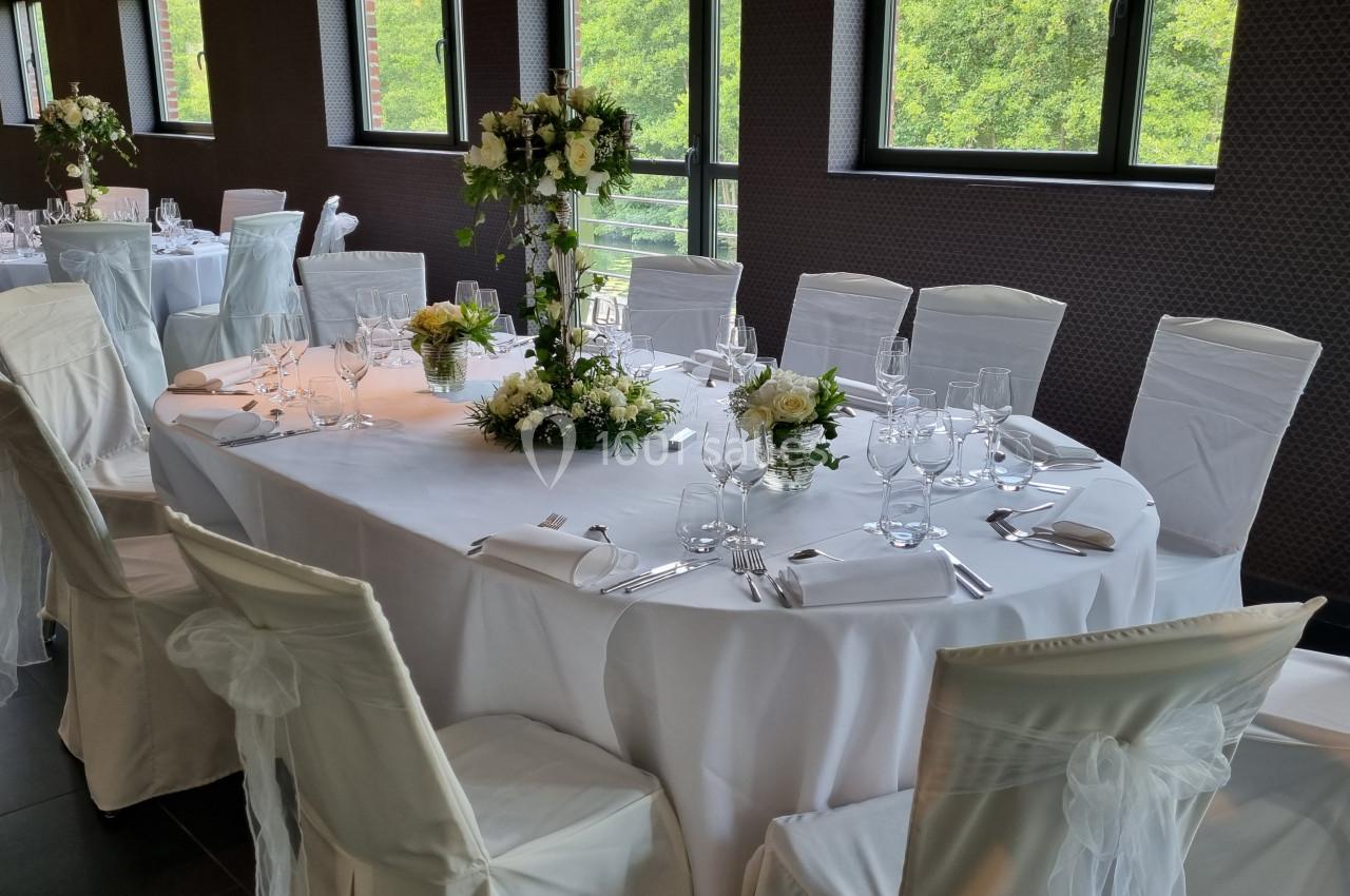 Table de réception élégamment dressée avec nappes blanches, chaises couvertes et centre de table floral.