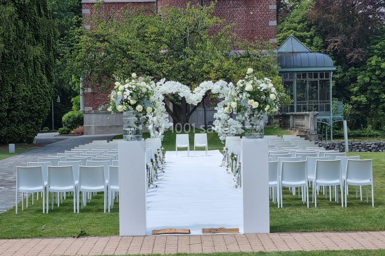 Allée décorée de fleurs blanches menant à une cérémonie en plein air, avec des chaises alignées devant un bâtiment en…
