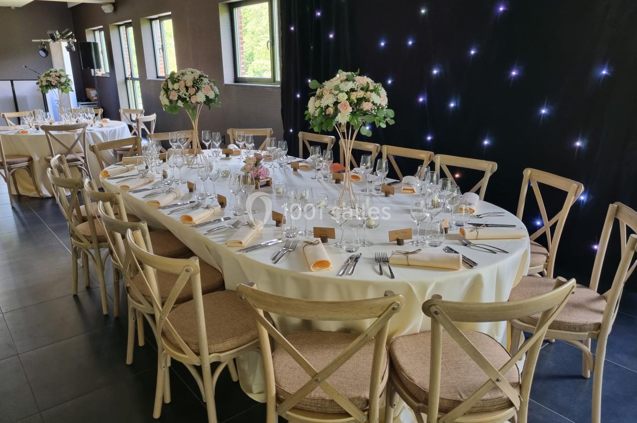 Grande table ronde élégamment dressée avec des chaises en bois, décorée de fleurs et entourée d'autres tables similaires.