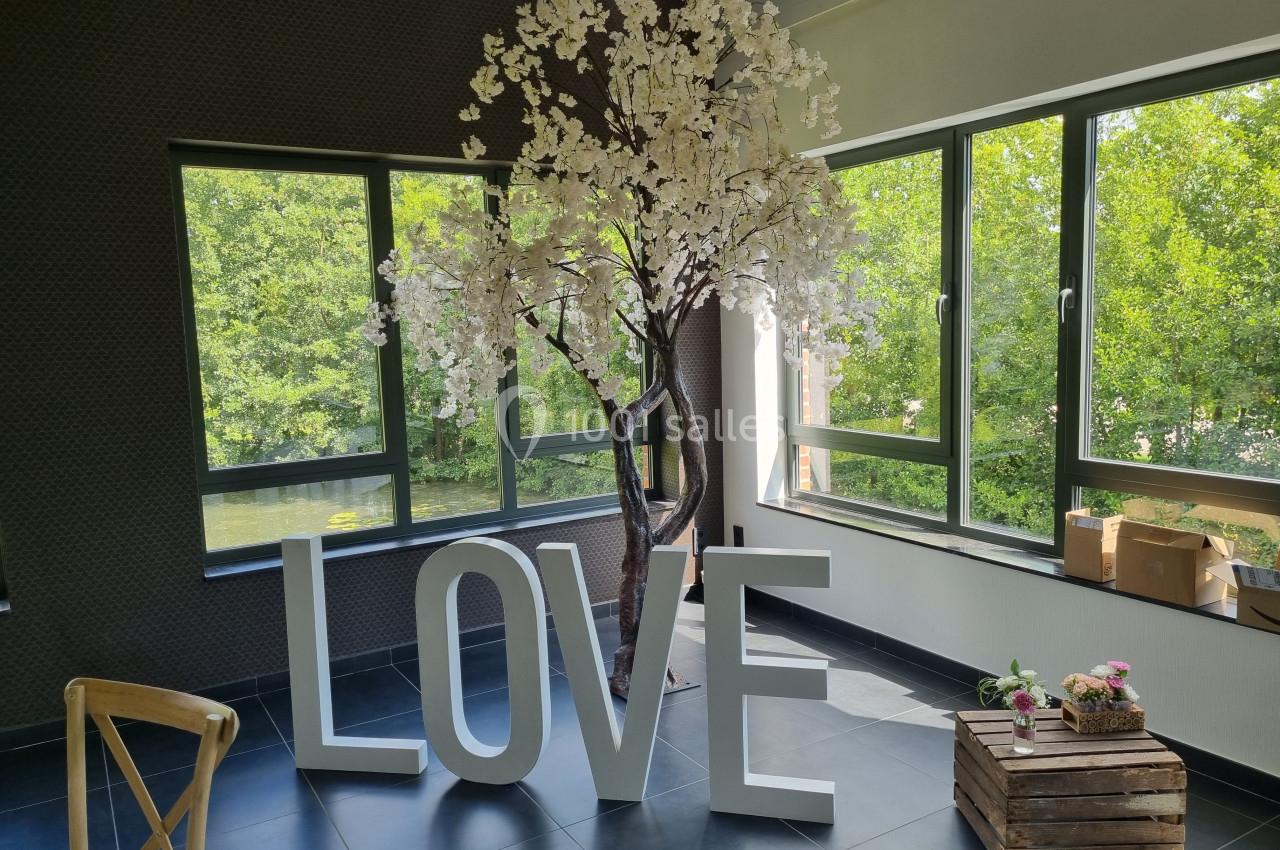 Arbre décoratif fleuri et grandes lettres formant ’LOVE’ dans une pièce lumineuse avec vue sur la verdure.