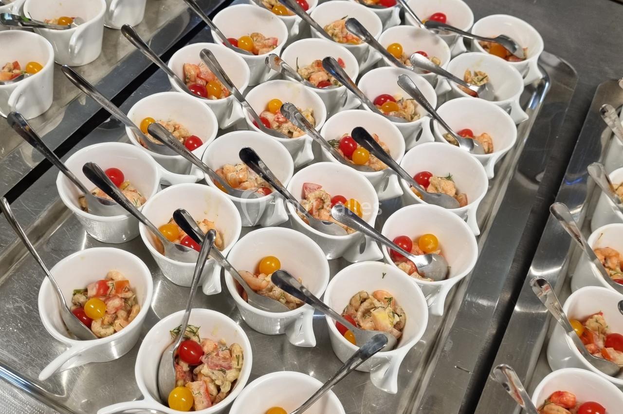 Petites verrines contenant des crevettes, tomates cerises et autres ingrédients, disposées sur un plateau en inox.