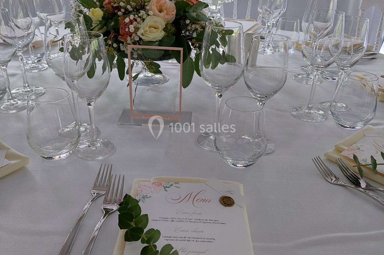 Table de réception élégamment dressée avec des fleurs, des bougies, des verres et un menu décoré de motifs floraux.
