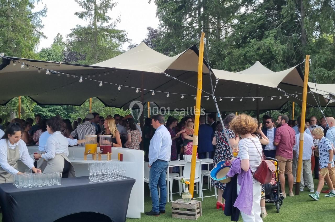 Groupe de personnes réunies sous une tente dans un jardin, avec des tables de service et des décorations lumineuses.