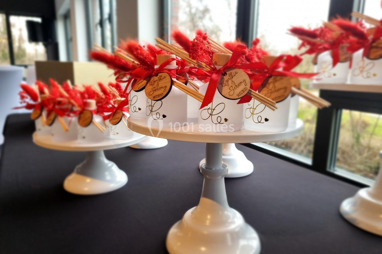 Présentoirs blancs décorés de bouquets rouges et étiquettes en bois, disposés sur une table près d'une fenêtre.