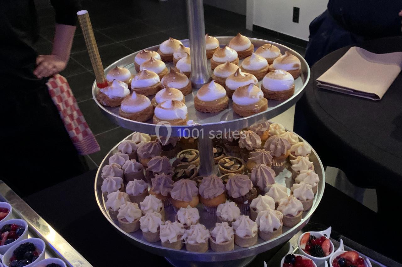 Plateau à étages avec divers desserts miniatures, entouré de verrines de fruits rouges sur une table.
