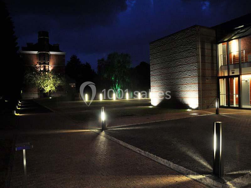 Allée pavée éclairée par des bornes lumineuses modernes, entourée de bâtiments et d'arbres sous un ciel nocturne.