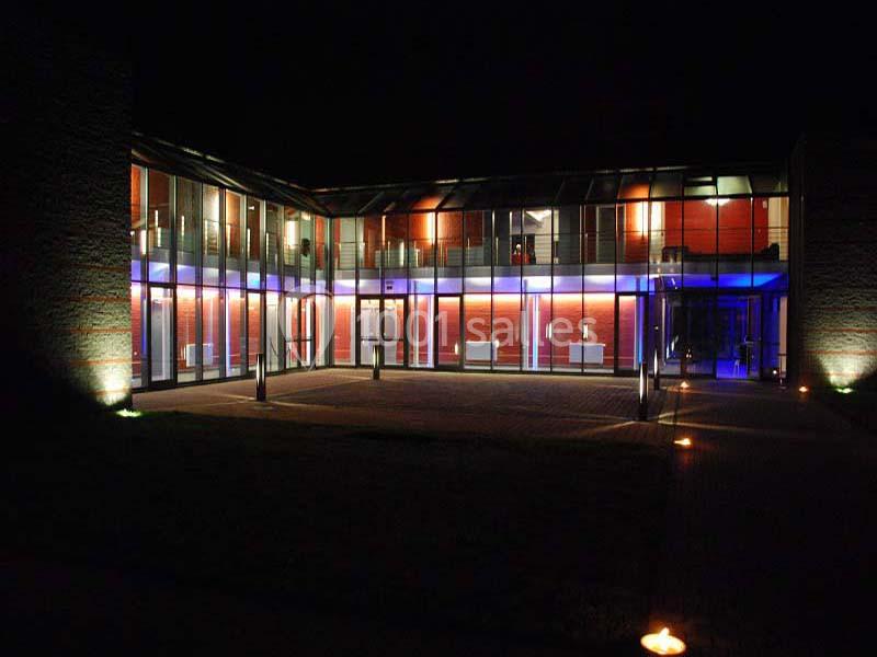 Façade vitrée d'un bâtiment moderne éclairé par des lumières bleues et jaunes, vue de nuit.