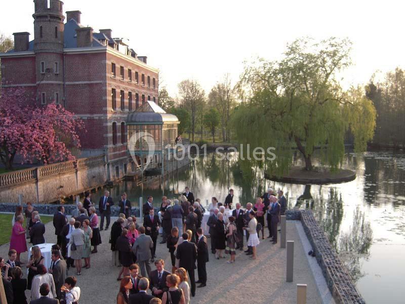 Groupe de personnes rassemblées près d'un bâtiment en briques rouges au bord d'un étang entouré d'arbres.