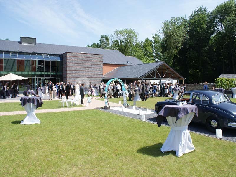 Groupe de personnes rassemblées à l'extérieur d'un bâtiment moderne lors d'un événement, avec tables dressées et une voiture…