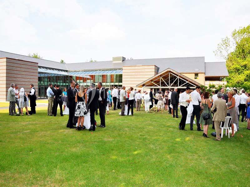 Groupe de personnes discutant dans un jardin devant un bâtiment moderne par une journée ensoleillée.