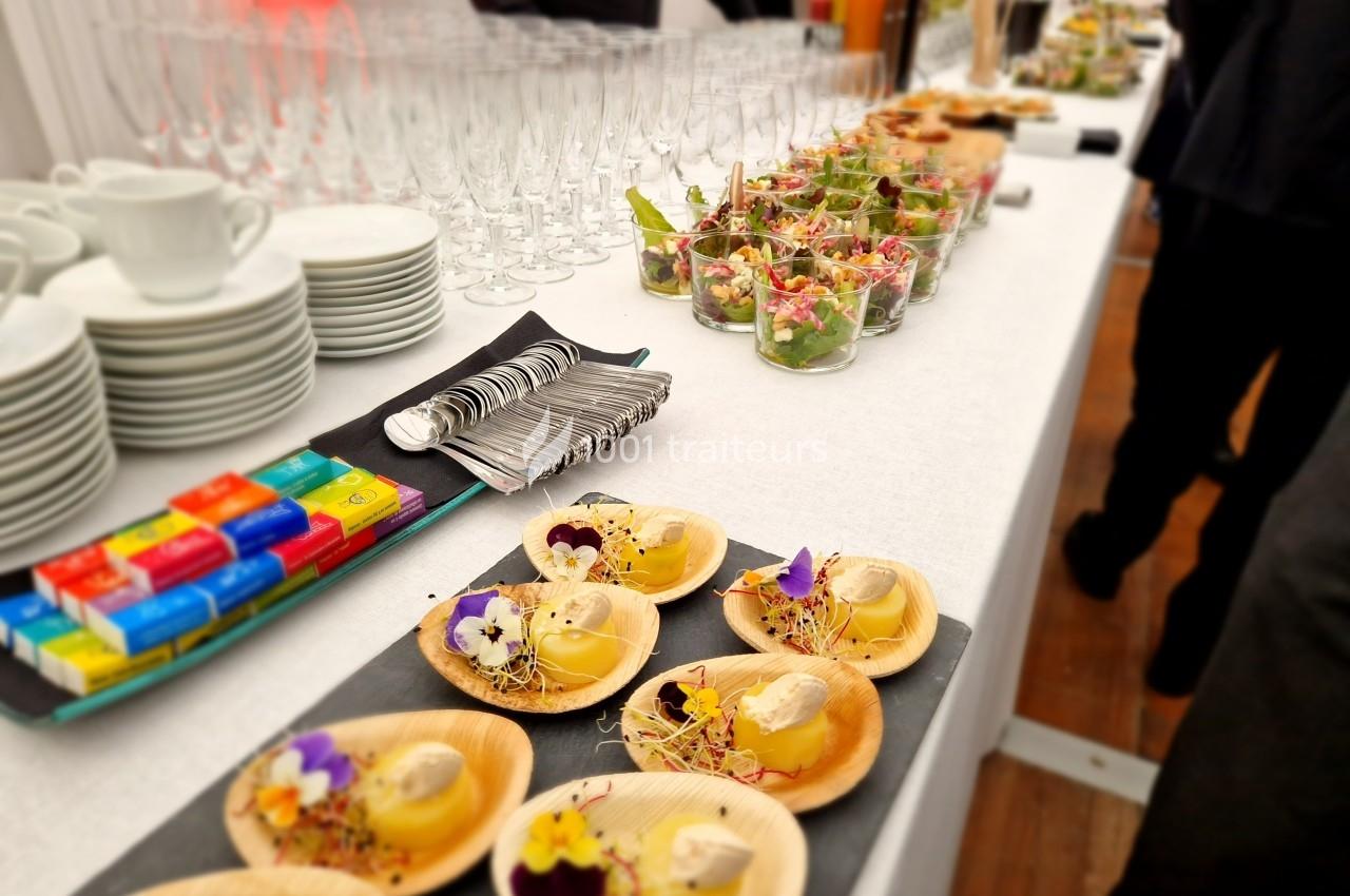 Buffet avec verrines, desserts décorés de fleurs comestibles, chocolats colorés, tasses et verres alignés.
