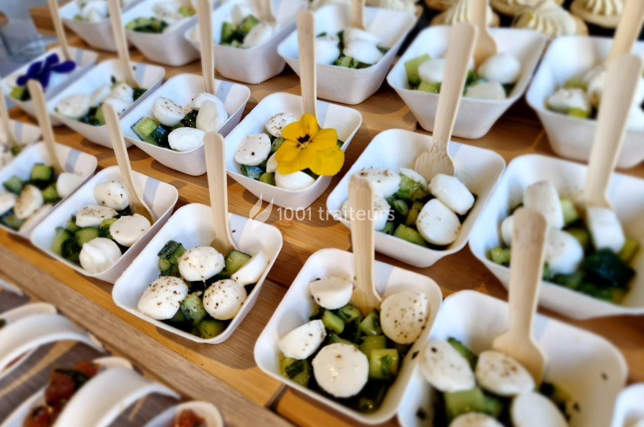 Petites assiettes en carton contenant des billes de mozzarella, des morceaux de concombre et des herbes, avec des cuillères…