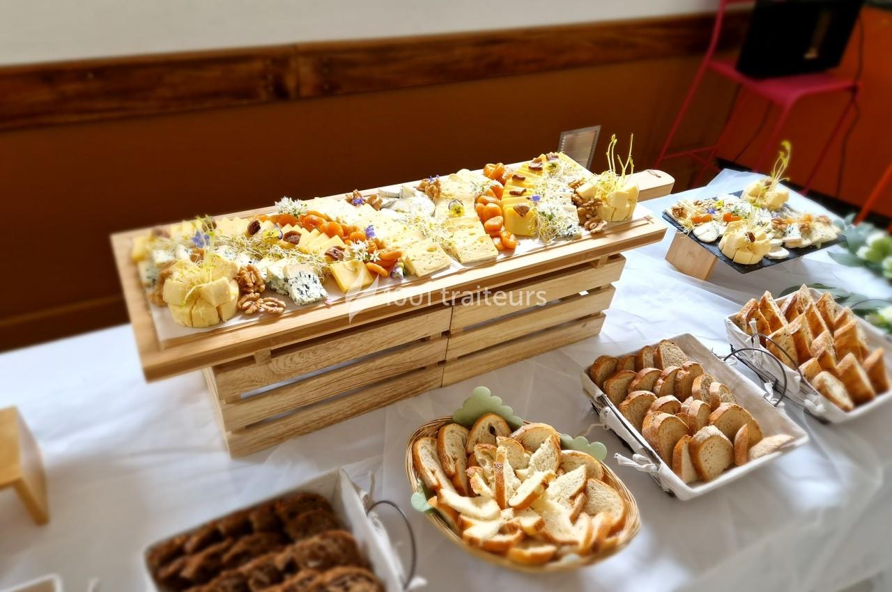 Plateau de fromages variés avec fruits secs et pain tranché disposé sur une table blanche pour un buffet.