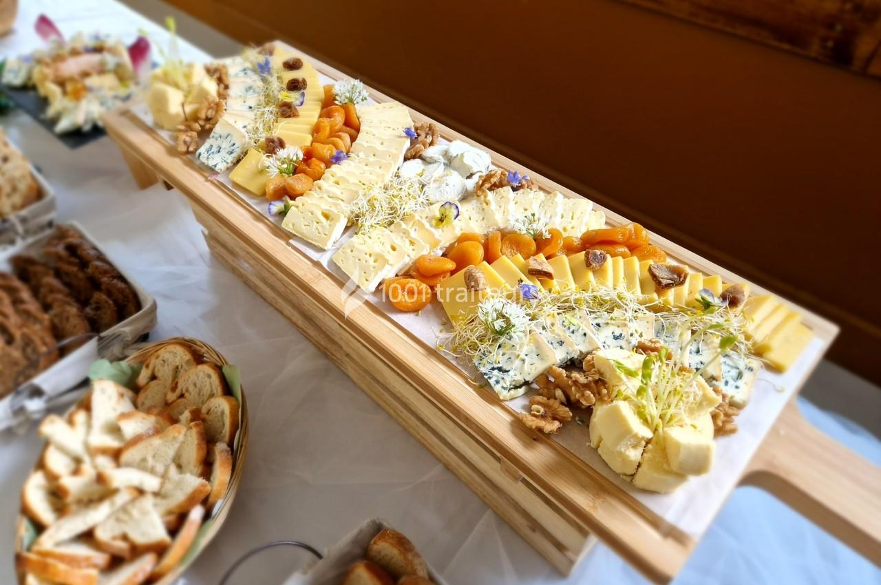 Plateau de fromages variés avec fruits secs, noix et herbes, accompagné de pains et viennoiseries sur une table.