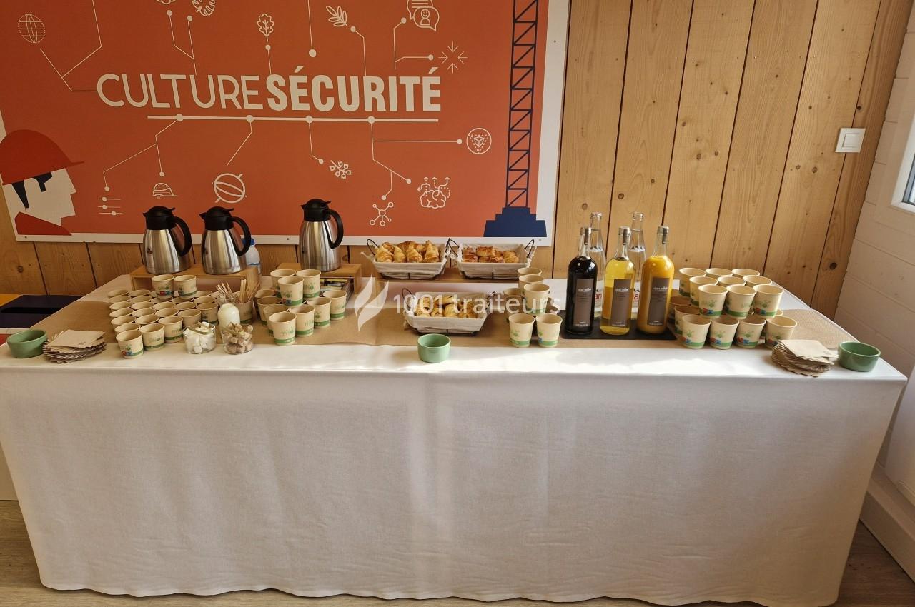 Table de buffet avec boissons chaudes, jus, viennoiseries et gobelets, devant un panneau ’Culture Sécurité’.