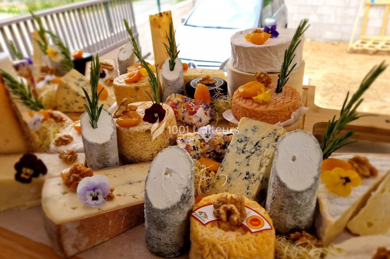 Plateau varié de fromages artisanaux décorés de fleurs comestibles, noix et herbes, présenté sur une table en bois.