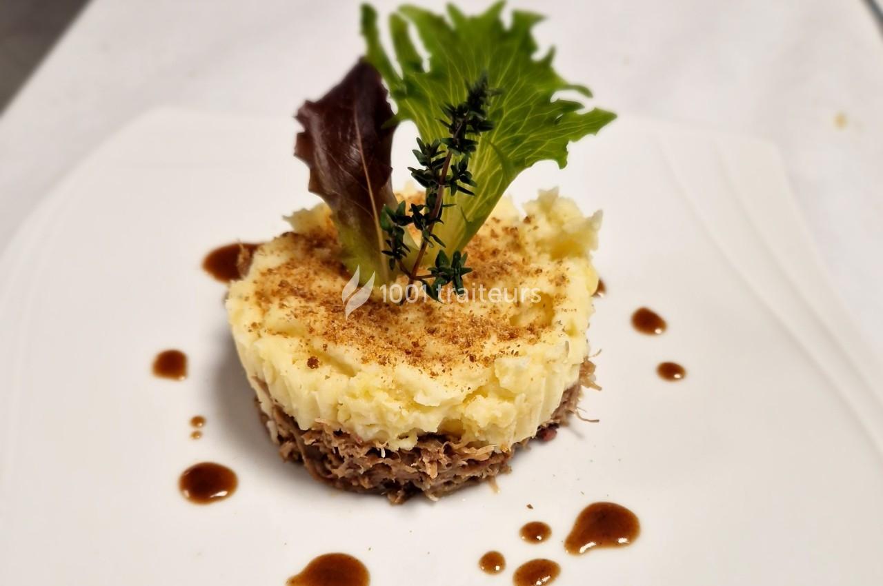 Plat dressé avec une base de viande effilochée, purée de pommes de terre, feuilles de salade et sauce en décoration.