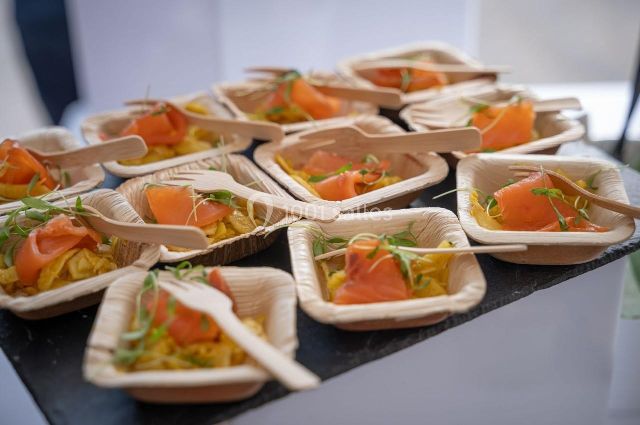 Assiettes individuelles en bois contenant des portions de saumon fumé, légumes et pousses vertes, avec des fourchettes en…