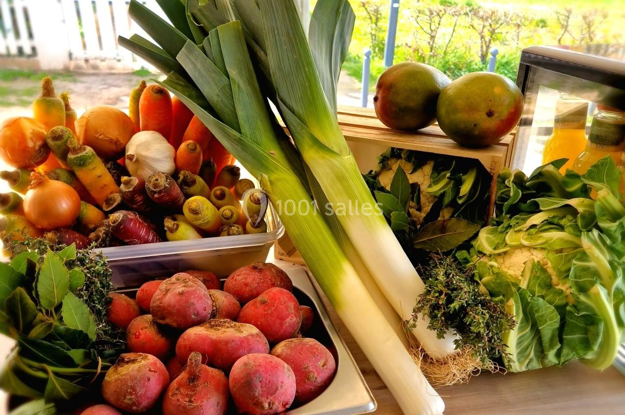 Légumes frais variés, dont poireaux, carottes, betteraves, choux et mangues, disposés sur une table en bois.