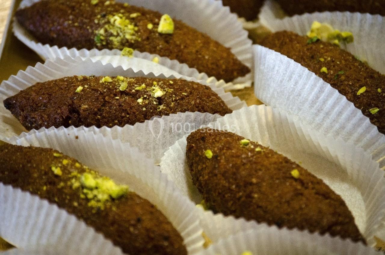 Pâtisseries ovales dorées garnies de pistaches, disposées dans des caissettes en papier blanc.