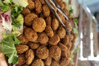 Assiette garnie de falafels dorés entourés de feuilles de salade et accompagnée de pinces en métal.