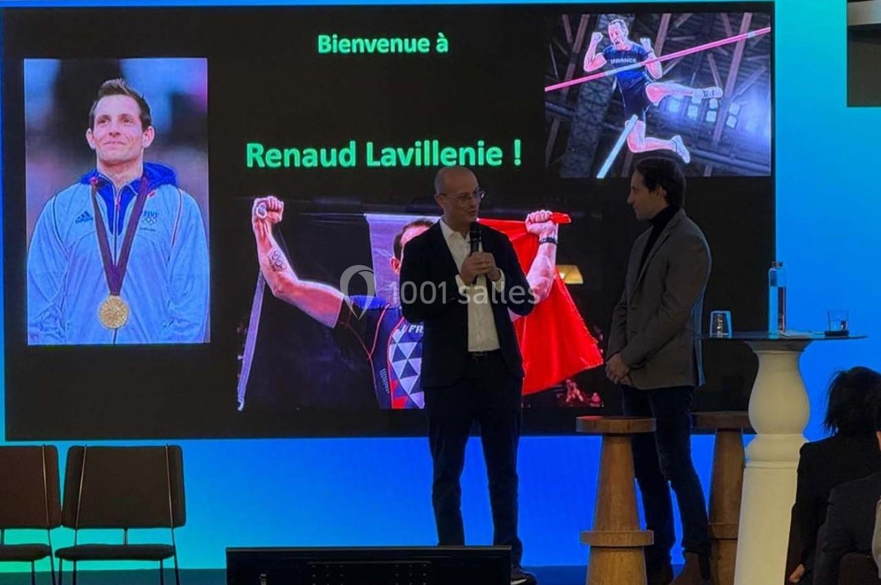 Photo Les Talents d'Espaces Réceptifs #2 Deux hommes discutent sur scène devant un écran affichant des images de Renaud Lavillenie et un message de bienvenue.