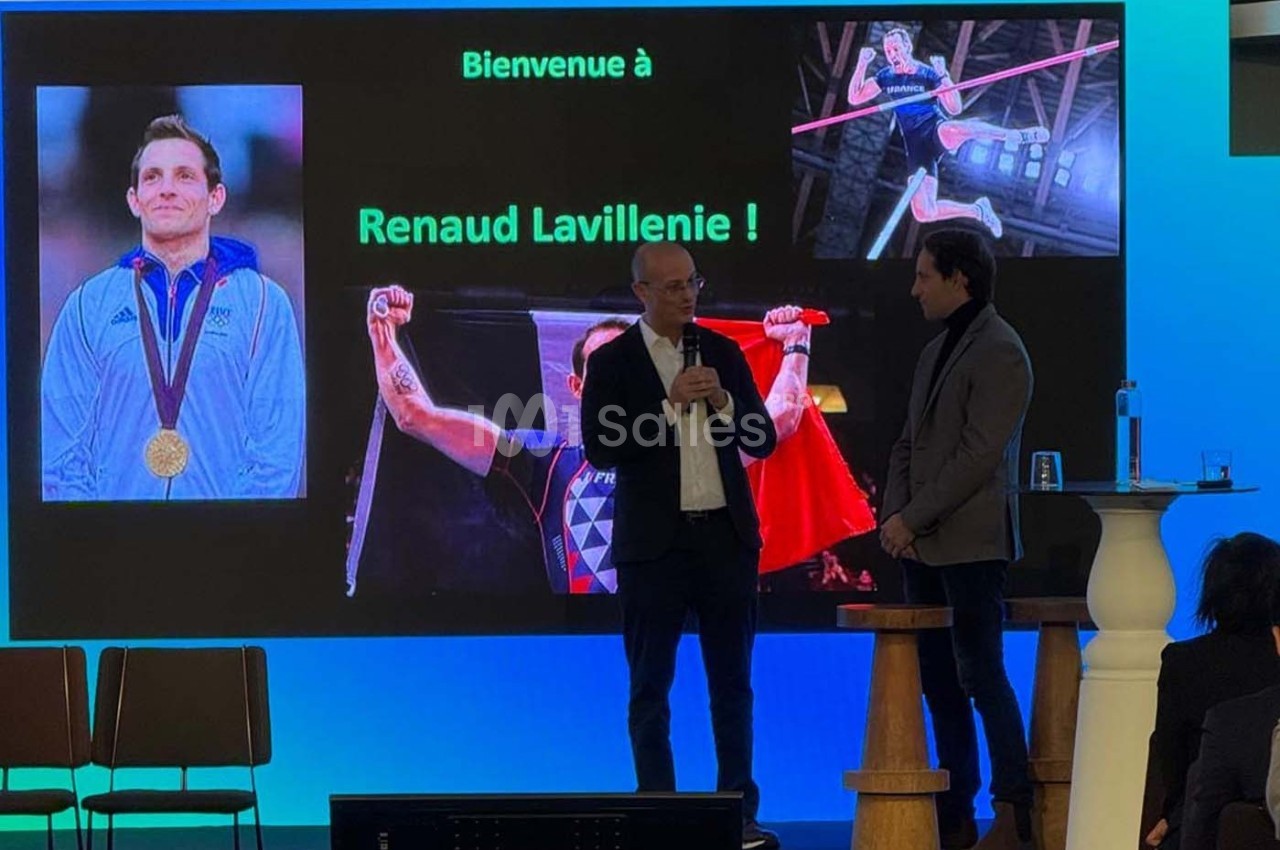 Deux hommes discutent sur scène devant un écran affichant des images de Renaud Lavillenie et un message de bienvenue.
