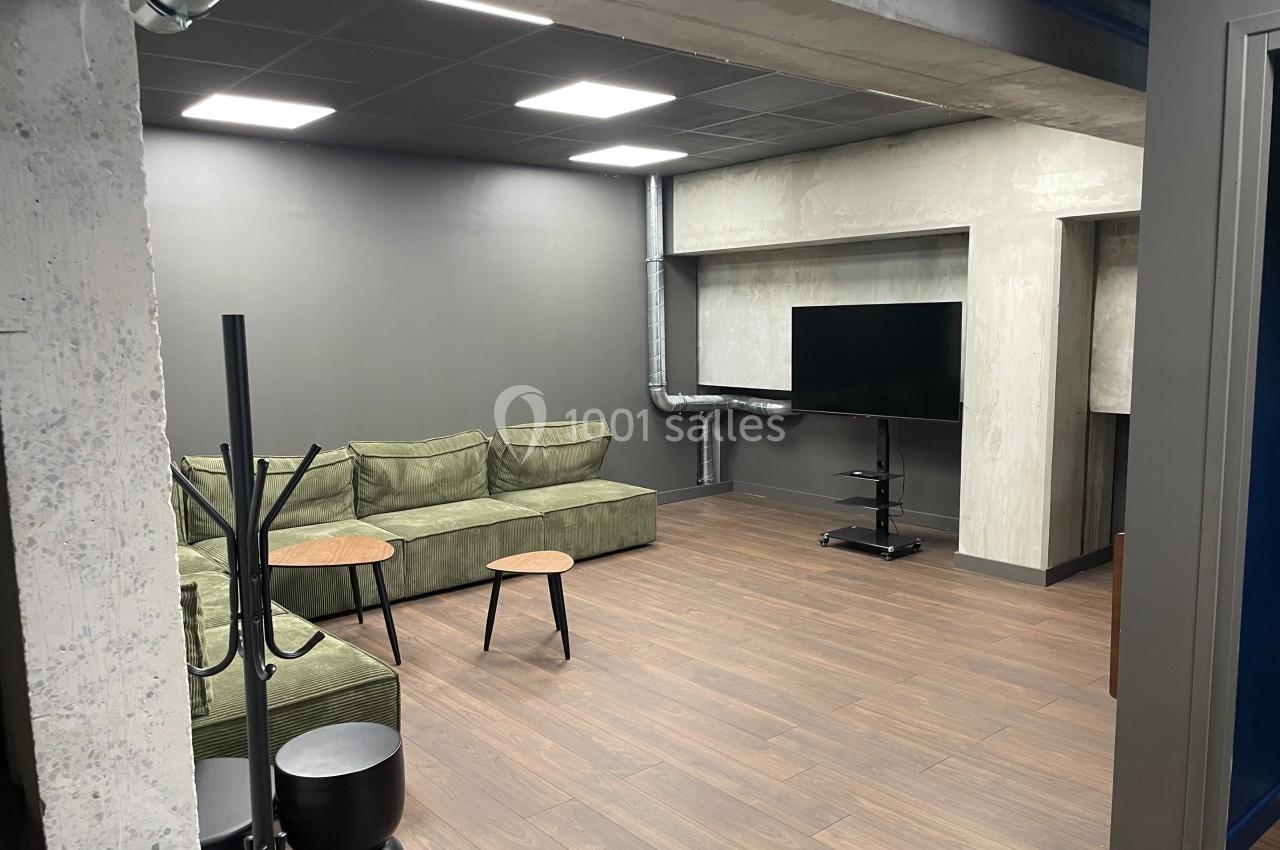Espace intérieur moderne avec canapé vert, tables basses en bois, sol en parquet et télévision sur pied.
