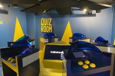 Salle de quiz interactive avec plusieurs bornes équipées d'écrans tactiles et de buzzers jaunes.