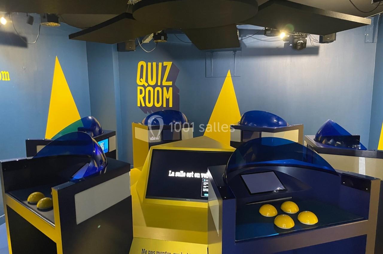 Salle de quiz interactive avec plusieurs bornes équipées d'écrans tactiles et de buzzers jaunes.