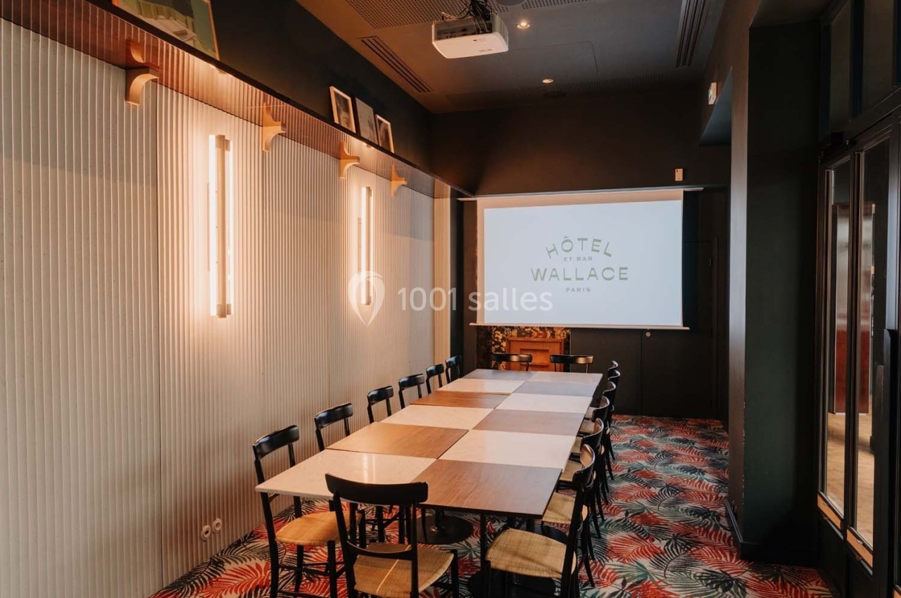 Salle de réunion lumineuse avec une grande table rectangulaire, des chaises en bois et un écran de projection.