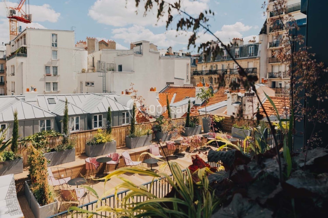 Vue d'une terrasse végétalisée avec des tables et des chaises, entourée de bâtiments urbains sous un ciel ensoleillé.
