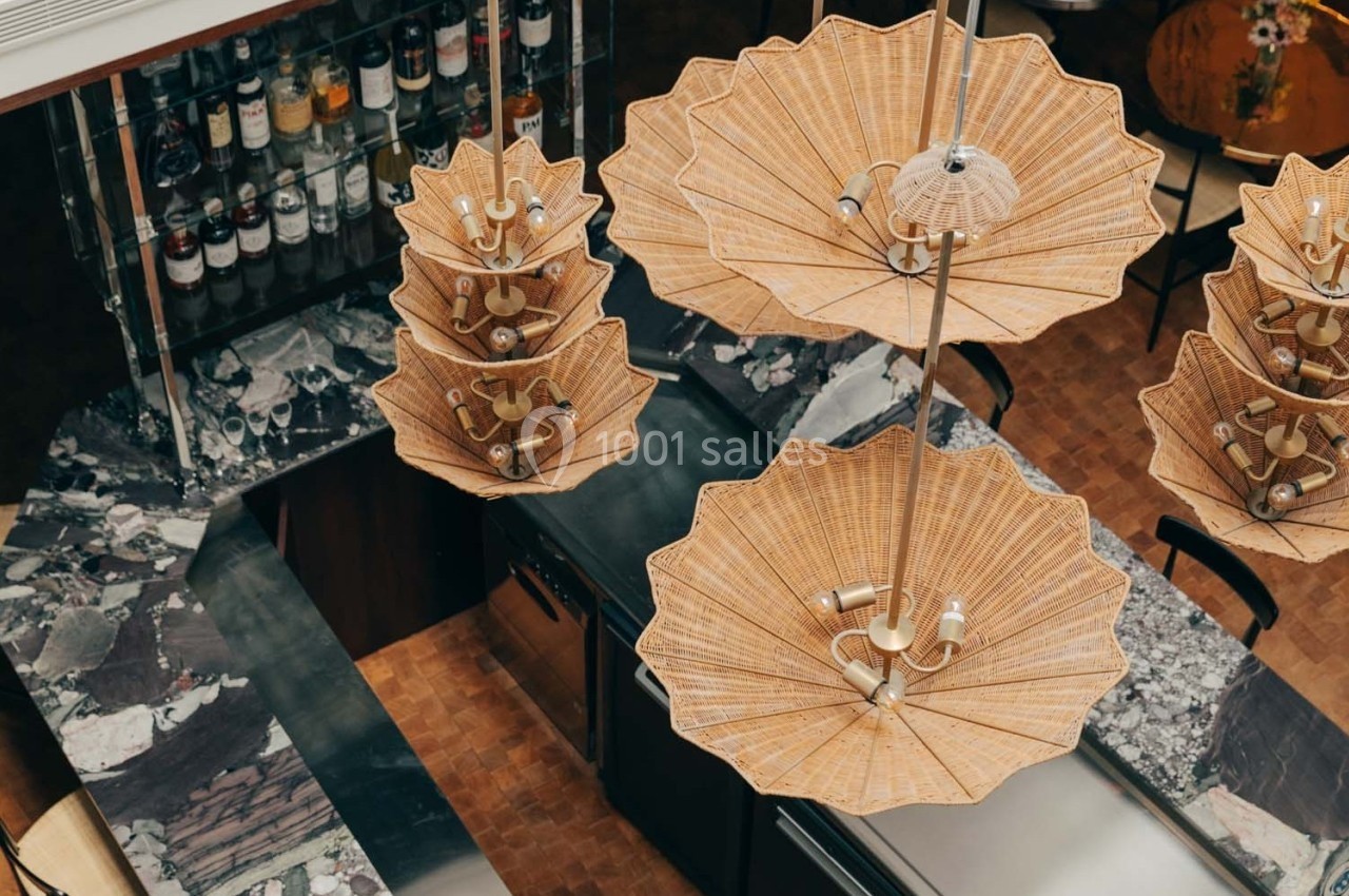 Suspensions en rotin au-dessus d'un comptoir en marbre sombre dans un espace intérieur élégant avec étagères à bouteilles.