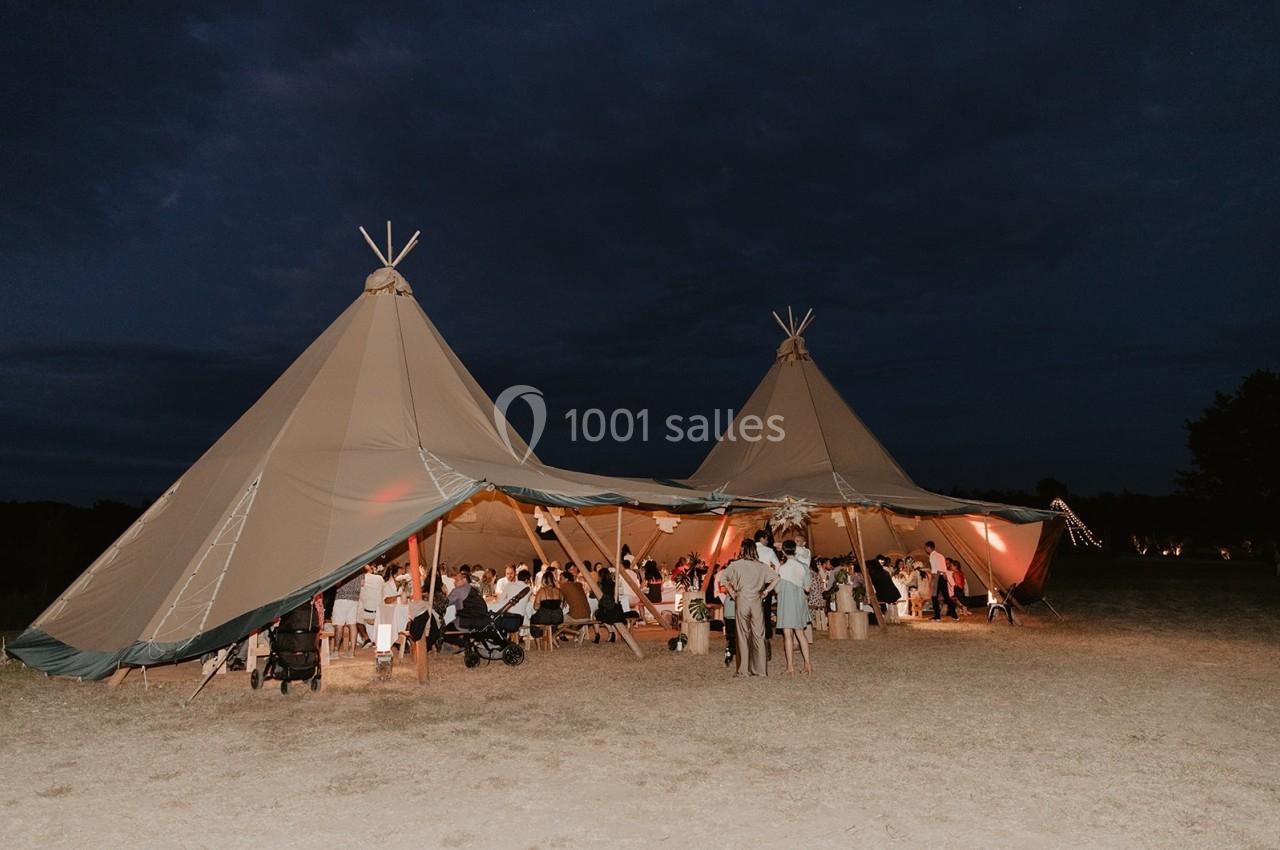 Deux grandes tentes tipi éclairées accueillent un rassemblement de personnes en soirée dans un espace extérieur.