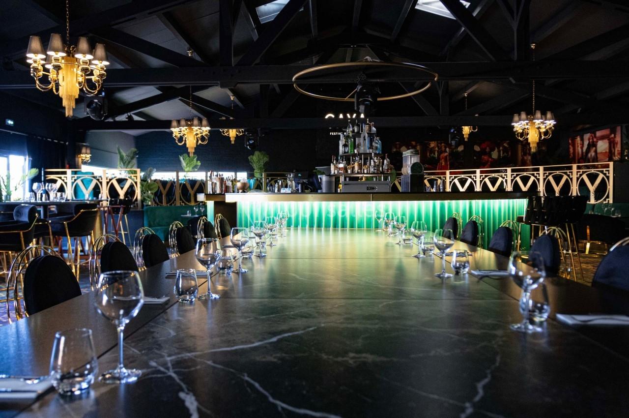Salle de restaurant élégante avec une longue table en marbre, bar lumineux en arrière-plan et décorations raffinées.