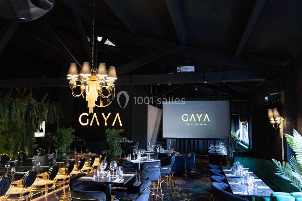 Salle de restaurant élégante avec tables dressées, éclairage tamisé, végétation et enseigne lumineuse ’Gaya’.