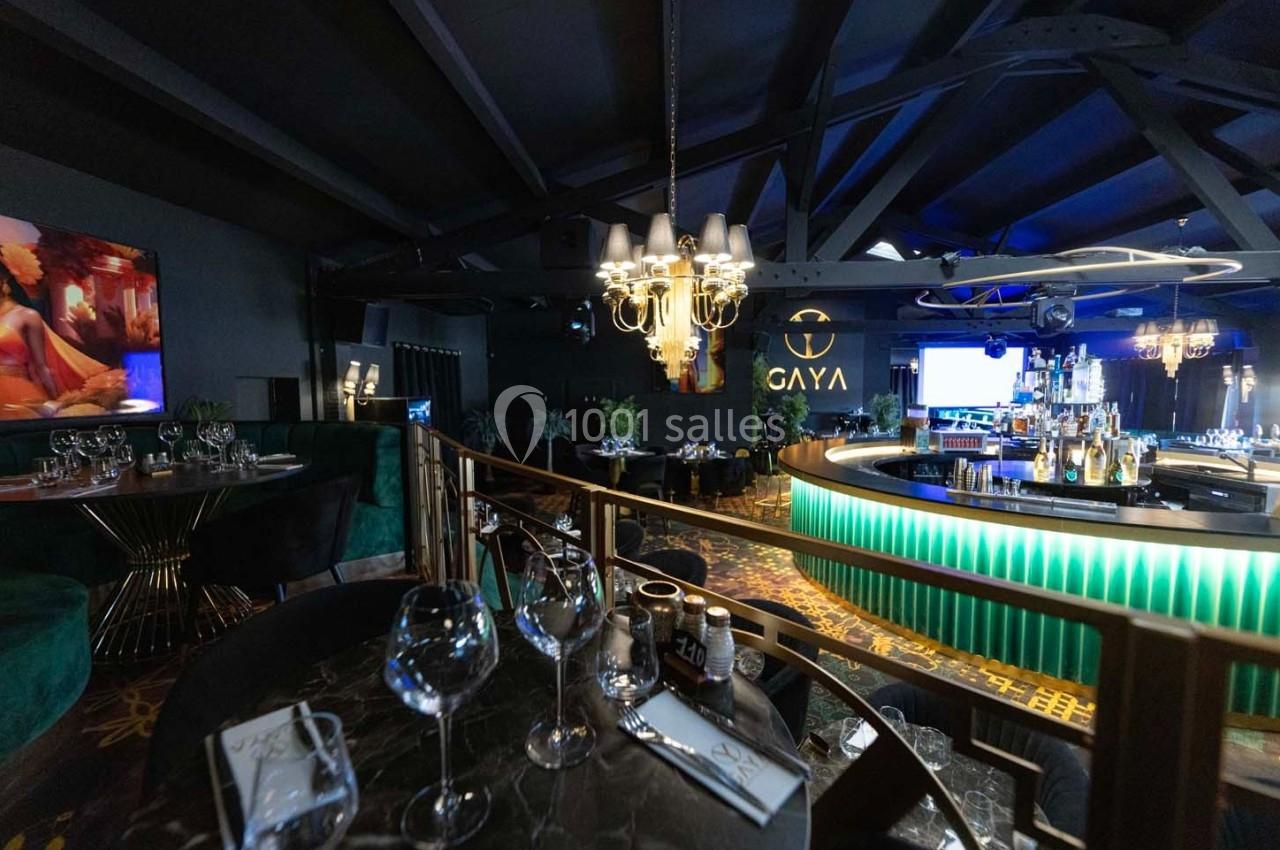 Salle de restaurant élégante avec bar central éclairé, tables dressées et ambiance tamisée sous un plafond sombre.