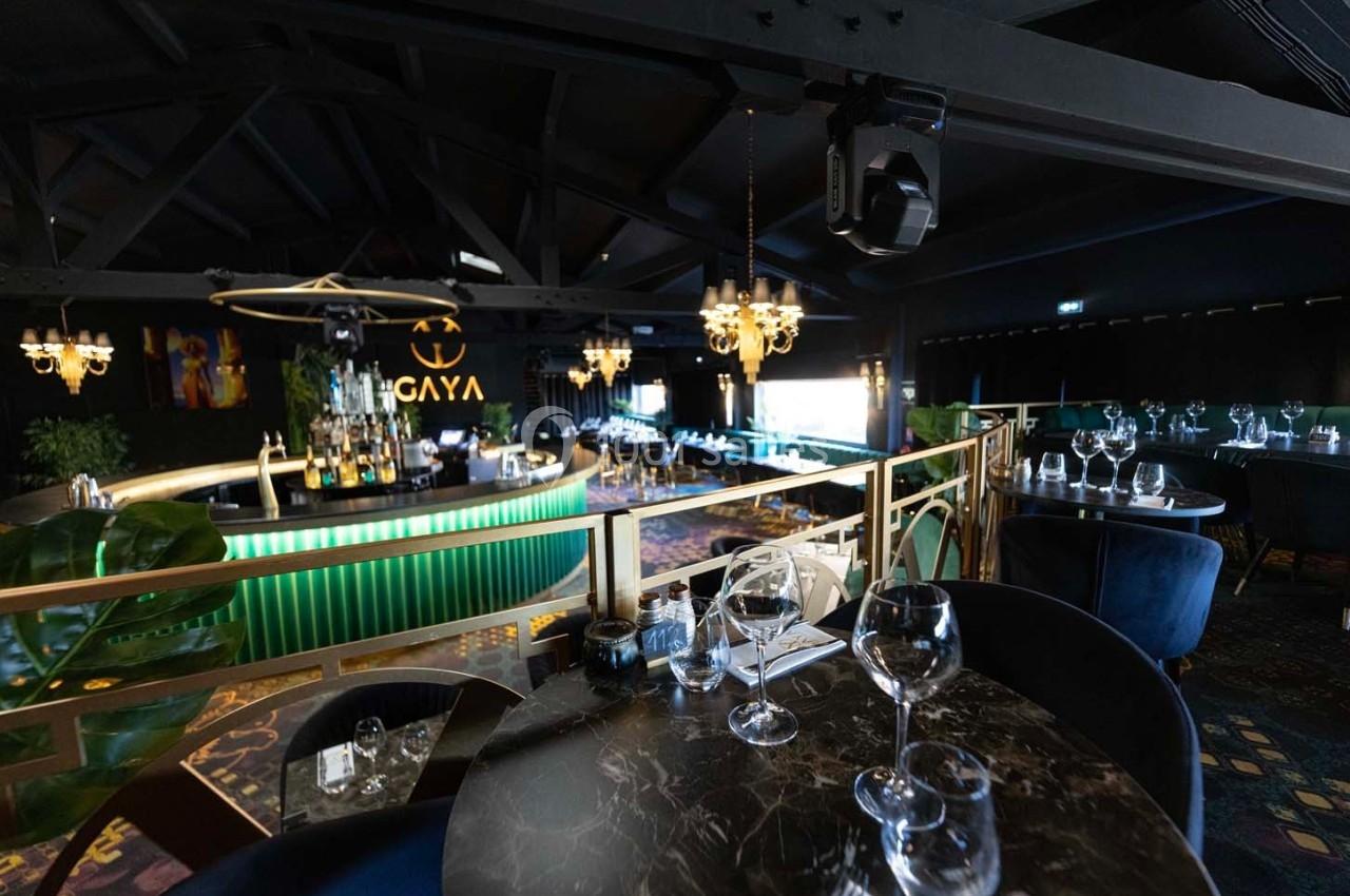Salle de restaurant élégante avec tables dressées, bar lumineux en arrière-plan et décorations modernes.