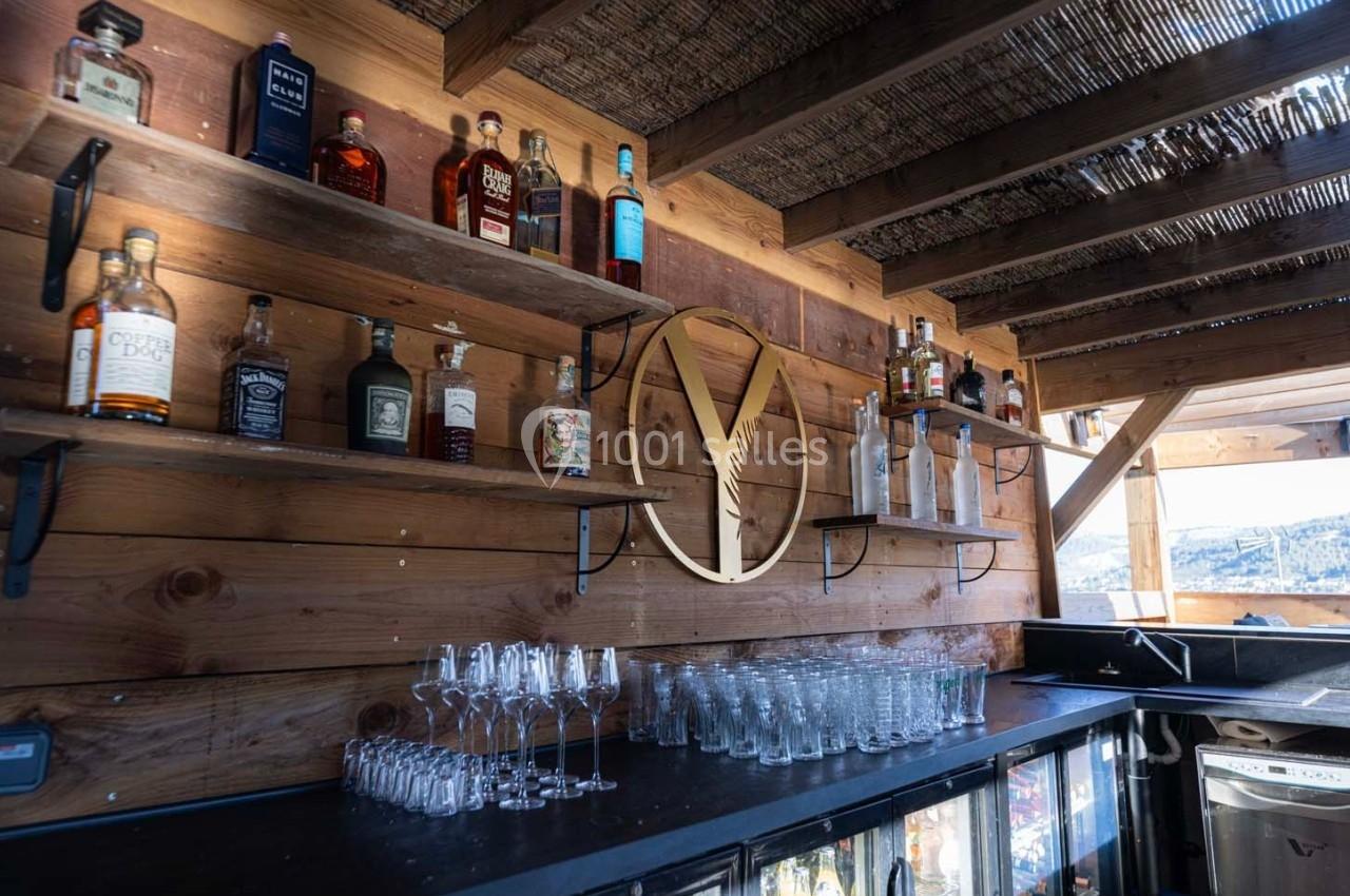 Étagères en bois garnies de bouteilles d'alcool et de verres, dans un bar extérieur à la structure en bois.
