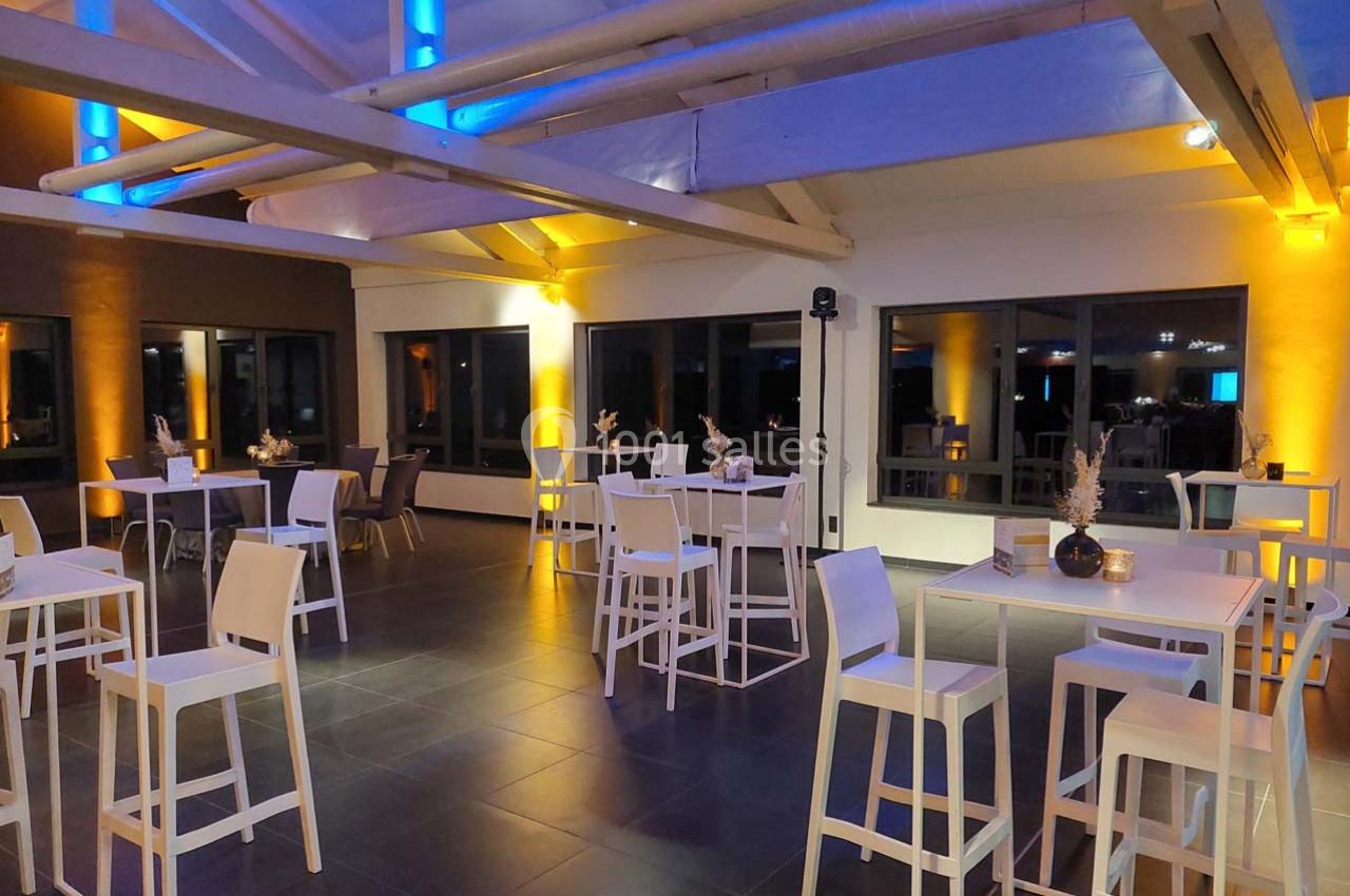 Salle moderne avec tables hautes blanches, chaises assorties et éclairage coloré bleu et jaune.