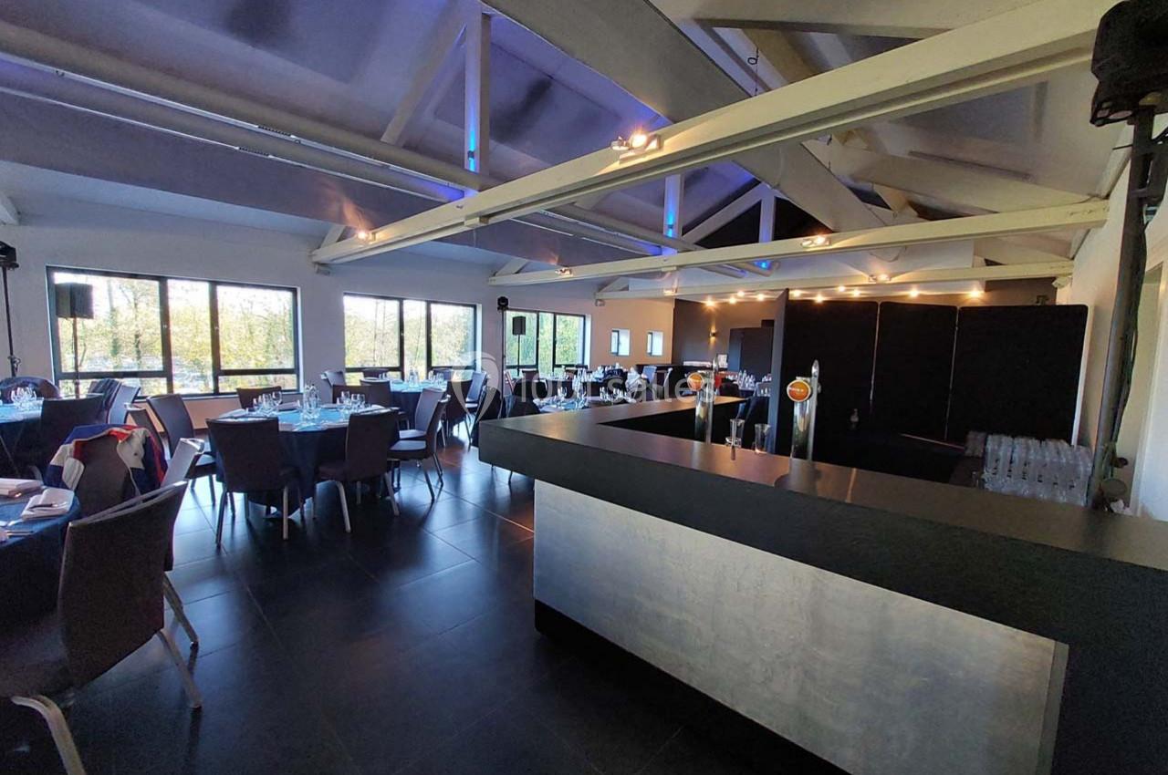 Salle moderne avec tables dressées, grandes baies vitrées, poutres apparentes et un comptoir au premier plan.