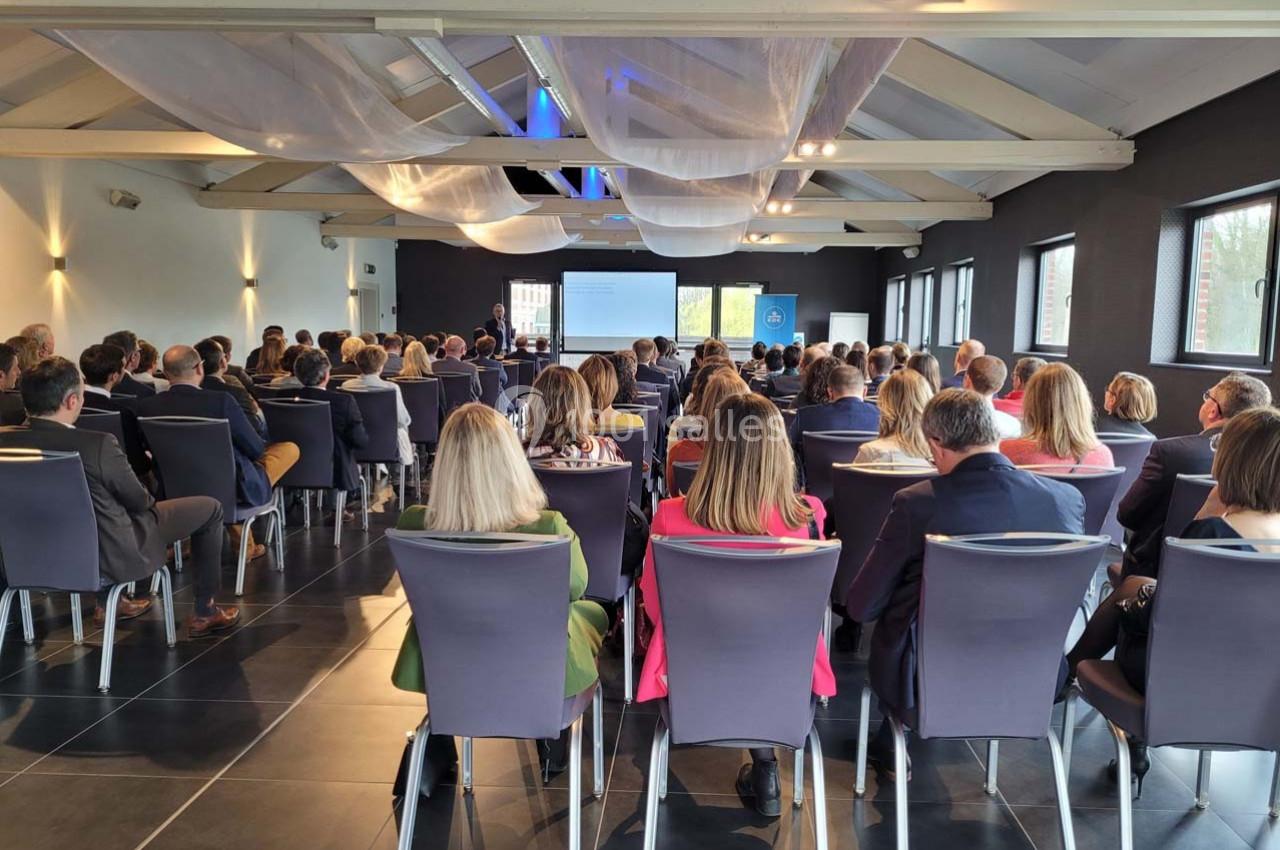 Salle de conférence avec un public assis écoutant une présentation projetée sur un écran à l'avant.
