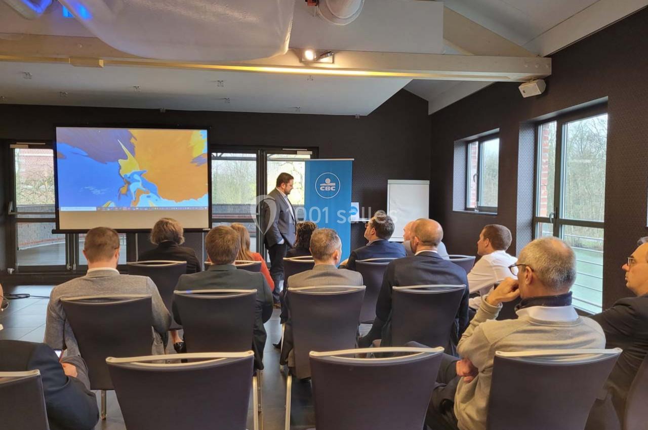 Un homme présente un diaporama devant un groupe de personnes assises dans une salle de conférence lumineuse.