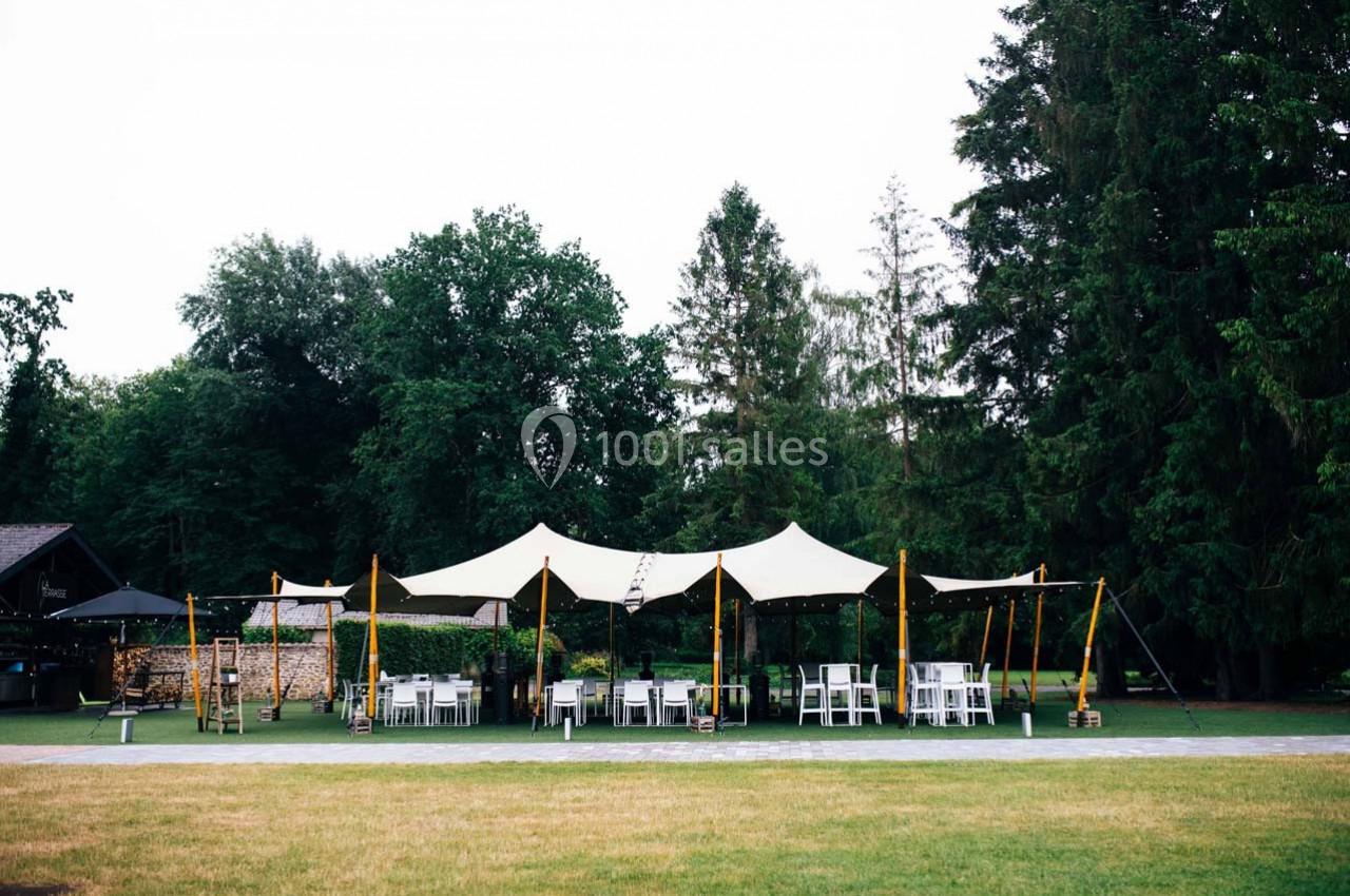 Tente blanche installée dans un jardin verdoyant, entourée de chaises et tables pour un événement en plein air.