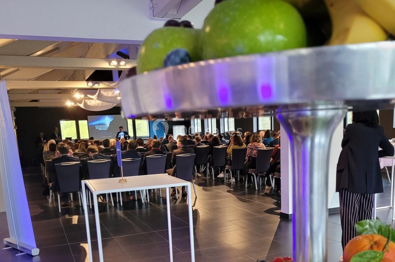 Vue d'une salle de conférence avec des participants assis, au premier plan un plateau de fruits colorés.