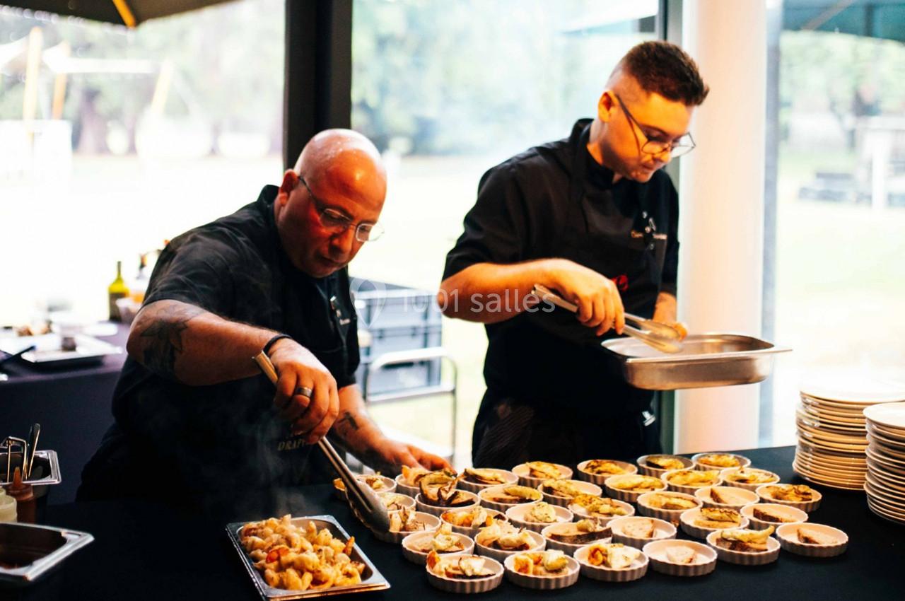 Deux chefs préparent et dressent des plats individuels dans une cuisine professionnelle lumineuse.