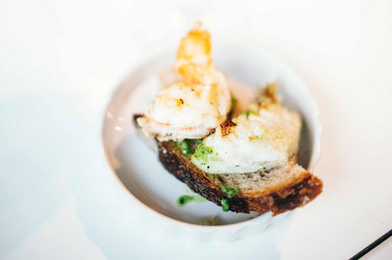 Crevette grillée et morceau de pain avec sauce verte, présentés dans une petite assiette blanche.