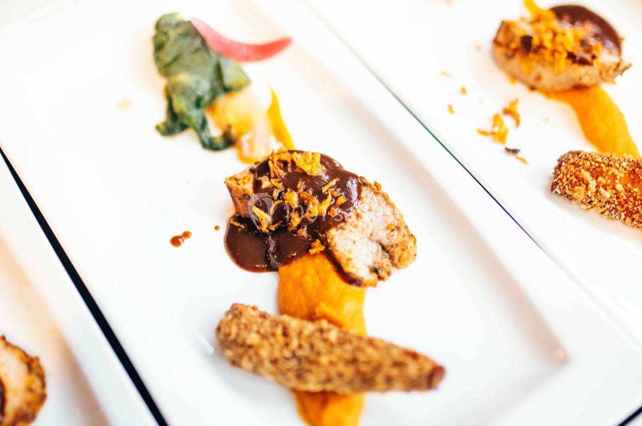 Assiette gastronomique avec viande, purée orange, légumes verts et croustillant, présentée sur une table blanche.